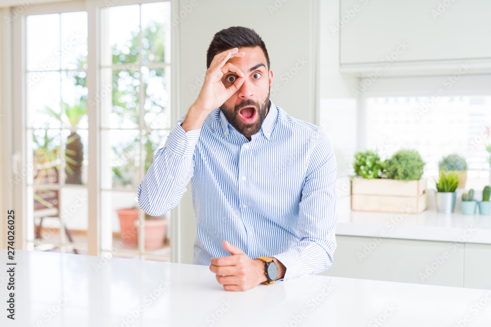 Fototapeta premium Handsome hispanic business man doing ok gesture shocked with surprised face, eye looking through fingers. Unbelieving expression.