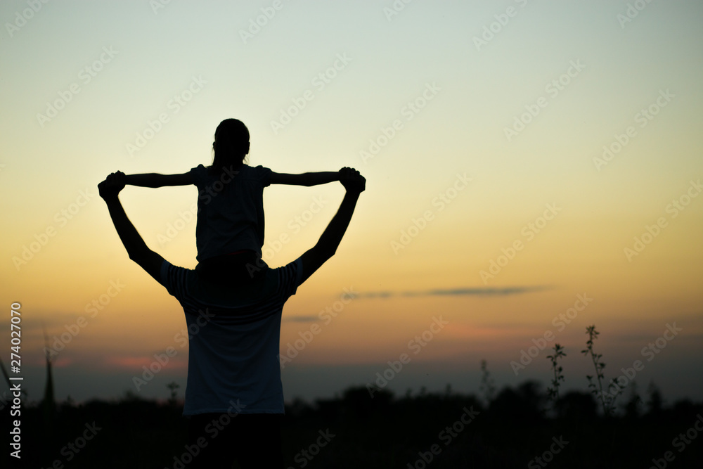 Silhouettes of father and daughter on his shoulders with hands up having fun, against sunset sky. Parenthood, family activities, beach holiday and vacation, support and love themes Silhouettes of father and daughter on his shoulders with hands up having fun, against sunset sky. Parenthood, family activities, beach holiday and vacation, support and love themes