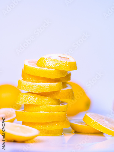 Yellow lemons cutted into slices on white background, close up view. Lemon juicy slices on light table, fruits composition. Blurred background. Selective soft focus