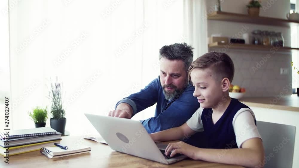Mature father with small son sitting at table indoors, working on school project. Mature father with small son sitting at table indoors, working on school project.