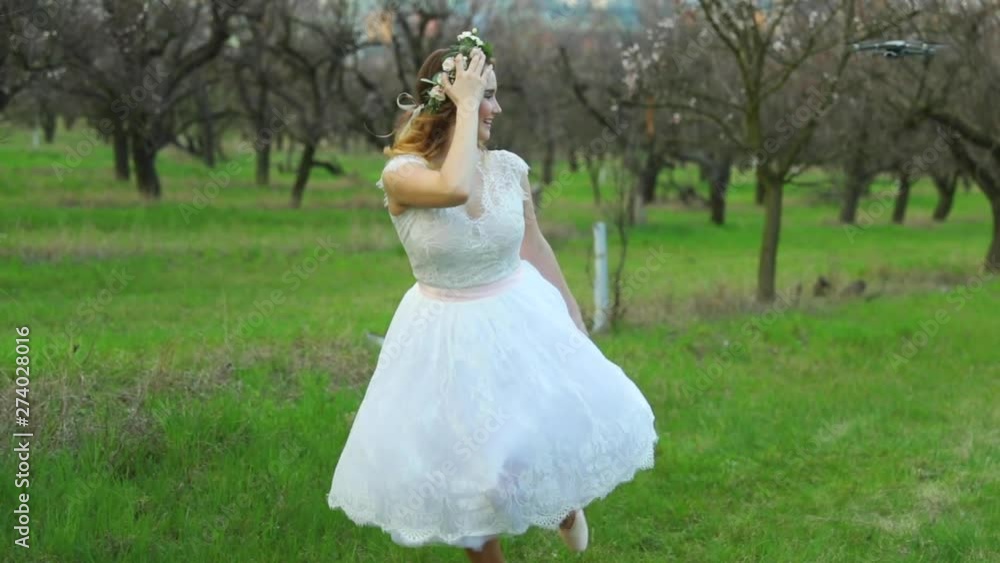 Ballerina in white wedding dress runs through apple orchard among trees in ballerinas outside on grass during spring day closeup view captured in 120 FPS Ballerina in white wedding dress runs through apple orchard among trees in ballerinas outside on grass during spring day closeup view captured in 120 FPS