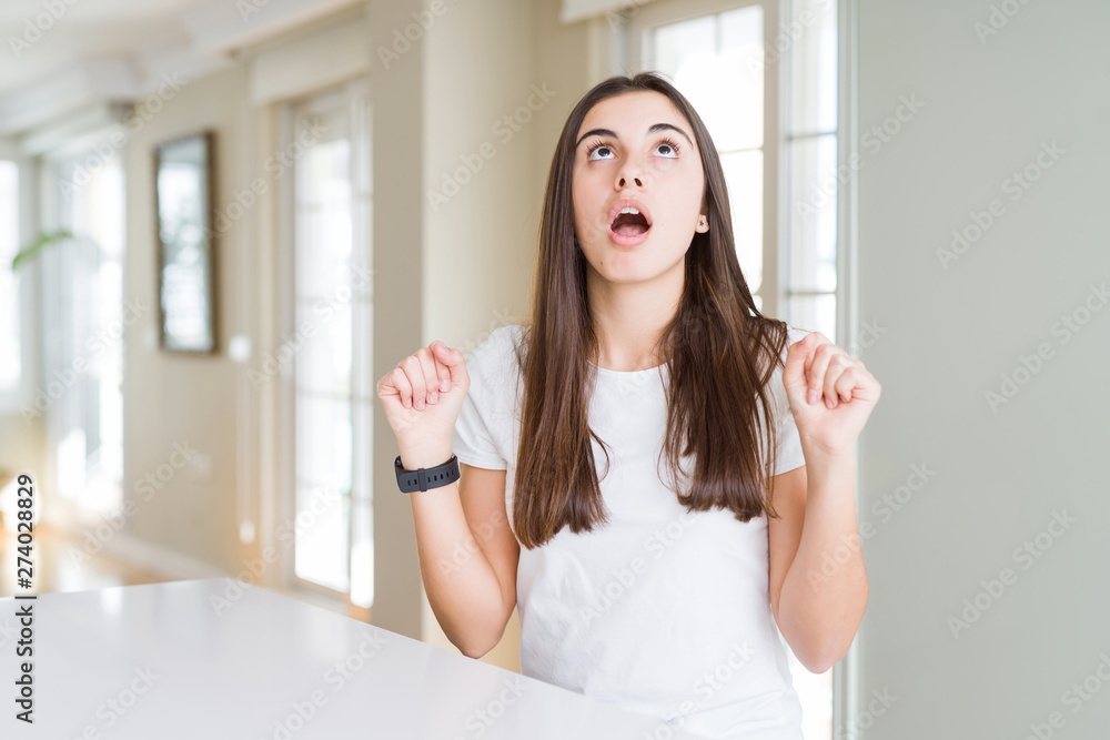 Beautiful young woman wearing casual white t-shirt amazed and surprised looking up and pointing with fingers and raised arms. Beautiful young woman wearing casual white t-shirt amazed and surprised looking up and pointing with fingers and raised arms.