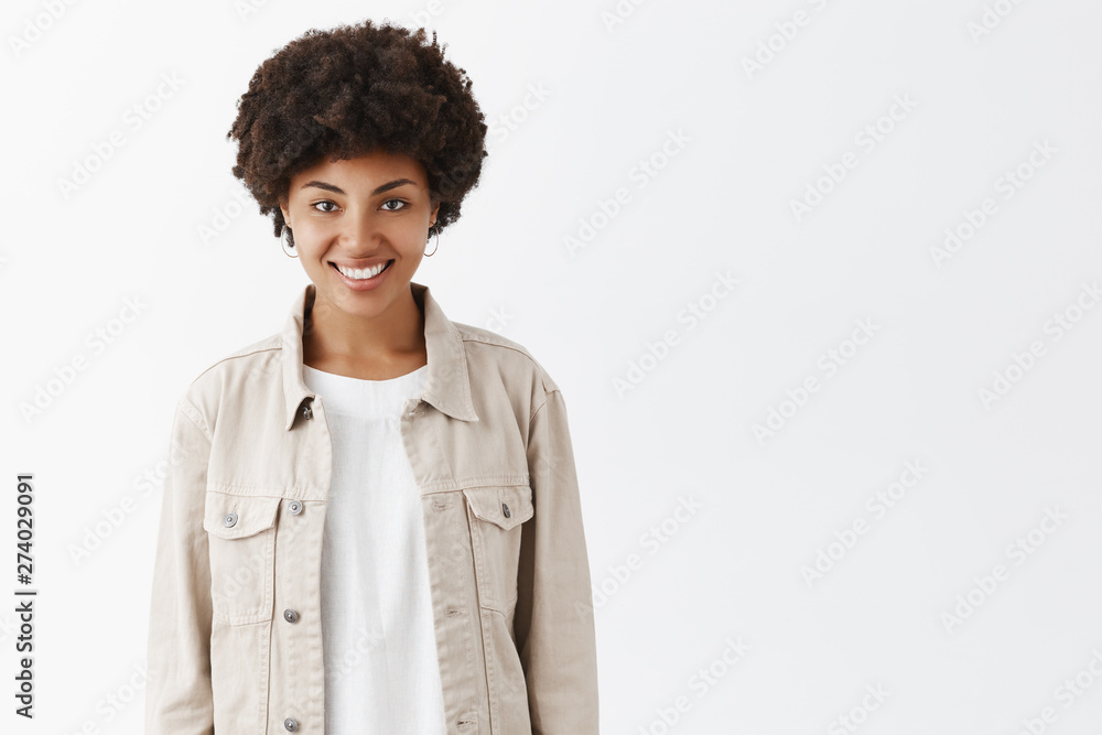 Indoor shot of cute tomboy girl with dark skin and afro hairstyle in trendy beige jacket over t-shirt, smiling broadly and gazing with self-assured and carefree expression, feeling happy and relaxed Indoor shot of cute tomboy girl with dark skin and afro hairstyle in trendy beige jacket over t-shirt, smiling broadly and gazing with self-assured and carefree expression, feeling happy and relaxed