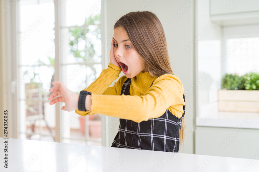 Young beautiful blonde kid girl wearing casual yellow sweater at home Looking at the watch time worried, afraid of getting late Young beautiful blonde kid girl wearing casual yellow sweater at home Looking at the watch time worried, afraid of getting late