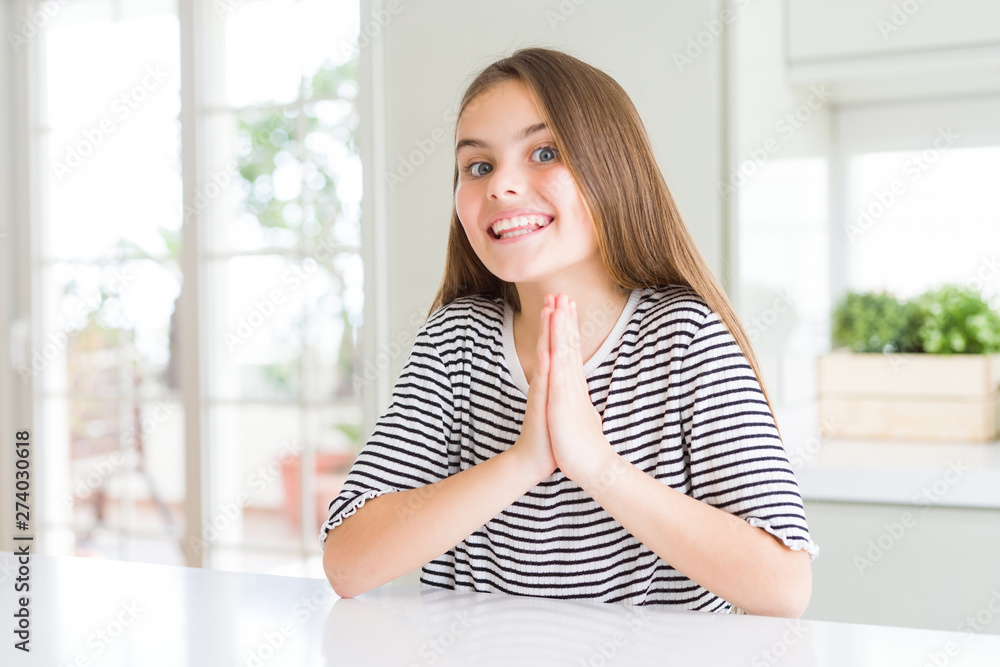 Beautiful young girl kid wearing stripes t-shirt praying with hands together asking for forgiveness smiling confident.