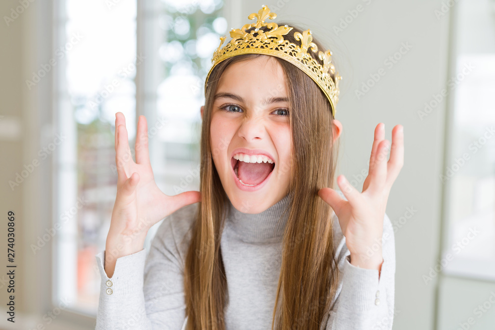 Beautiful young girl wearing a golden crown as a princess from fairytale celebrating mad and crazy for success with arms raised and closed eyes screaming excited. Winner concept Beautiful young girl wearing a golden crown as a princess from fairytale celebrating mad and crazy for success with arms raised and closed eyes screaming excited. Winner concept