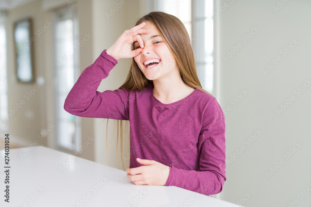 Beautiful young girl kid on white table doing ok gesture with hand smiling, eye looking through fingers with happy face. Beautiful young girl kid on white table doing ok gesture with hand smiling, eye looking through fingers with happy face.