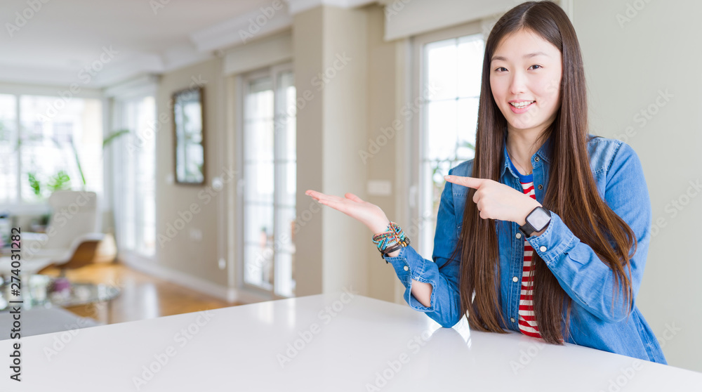 Young beautiful asian woman with long hair wearing denim jacket amazed and smiling to the camera while presenting with hand and pointing with finger. Young beautiful asian woman with long hair wearing denim jacket amazed and smiling to the camera while presenting with hand and pointing with finger.