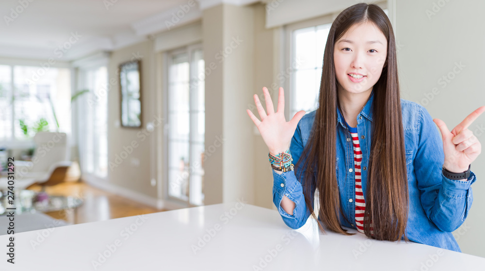 Young beautiful asian woman with long hair wearing denim jacket showing and pointing up with fingers number seven while smiling confident and happy.