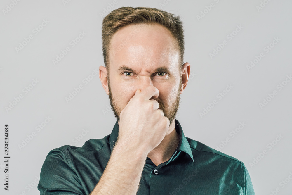 Portrait of guy, covering nose with fingers over gray background Portrait of guy, covering nose with fingers over gray background