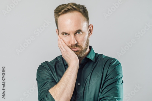Very bored adult man with beard holding hand on cheek looking tired and sick