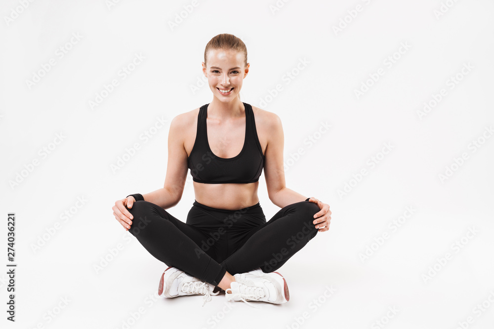 Image of nice sporty woman wearing tracksuit sitting on floor with legs crossed