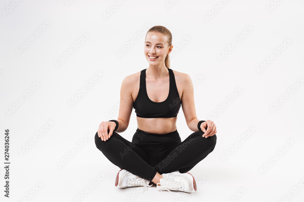 Image of pretty sporty woman wearing tracksuit sitting on floor with legs crossed Image of pretty sporty woman wearing tracksuit sitting on floor with legs crossed