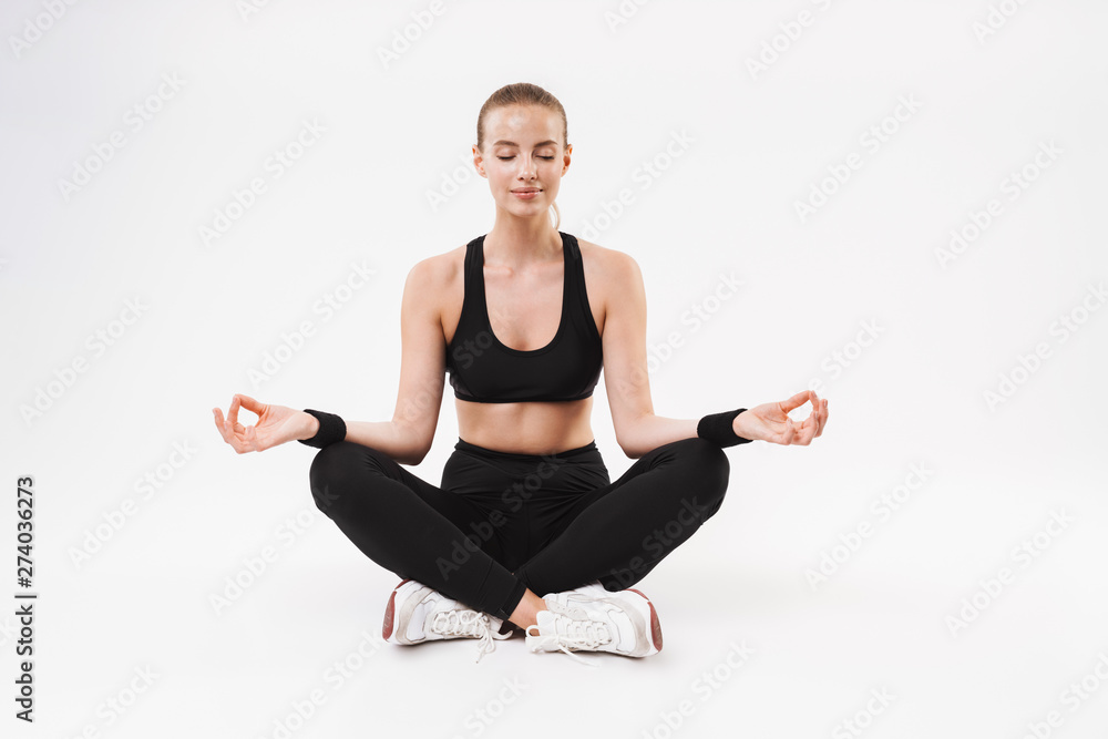 Image of sporty calm woman wearing tracksuit meditating with eyes closed and zen fingers while sitting on floor