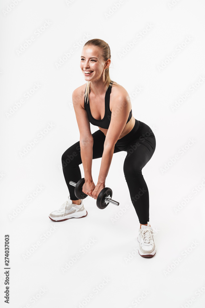 Image of beautiful strong woman wearing tracksuit smiling while lifting dumbbell during workout
