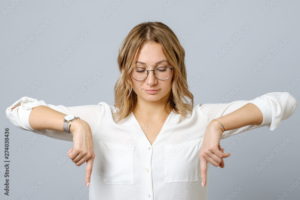 Portrait of young woman dressed in white pointing fingers down Portrait of young woman dressed in white pointing fingers down