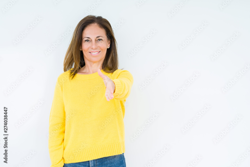 Beautiful middle age woman wearing yellow sweater over isolated background smiling friendly offering handshake as greeting and welcoming. Successful business. Beautiful middle age woman wearing yellow sweater over isolated background smiling friendly offering handshake as greeting and welcoming. Successful business.