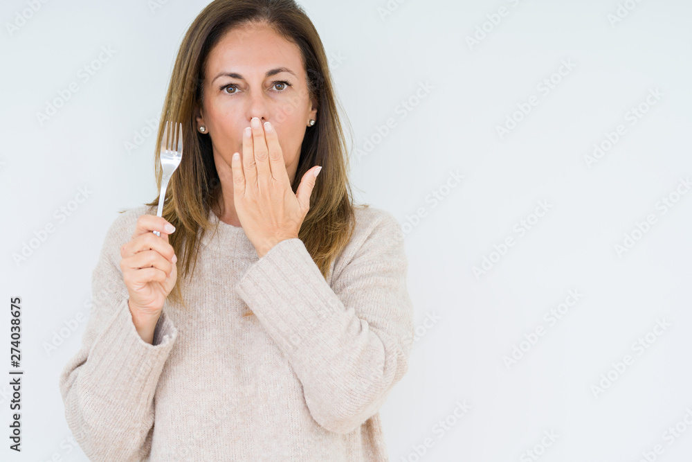 Middle age woman holding silver fork metal over isolated background cover mouth with hand shocked with shame for mistake, expression of fear, scared in silence, secret concept Middle age woman holding silver fork metal over isolated background cover mouth with hand shocked with shame for mistake, expression of fear, scared in silence, secret concept