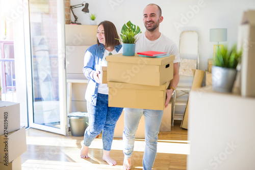 Young couple moving to a new home, smiling happy holding cardboard boxes