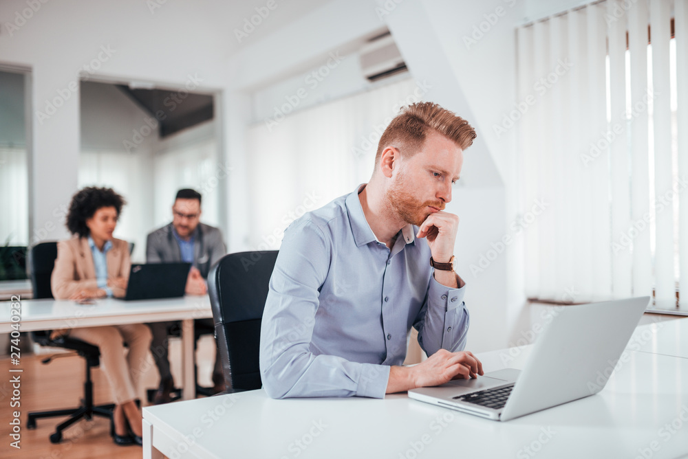 Puzzled redhead businessman looking at laptop screen in co working office. Puzzled redhead businessman looking at laptop screen in co working office.