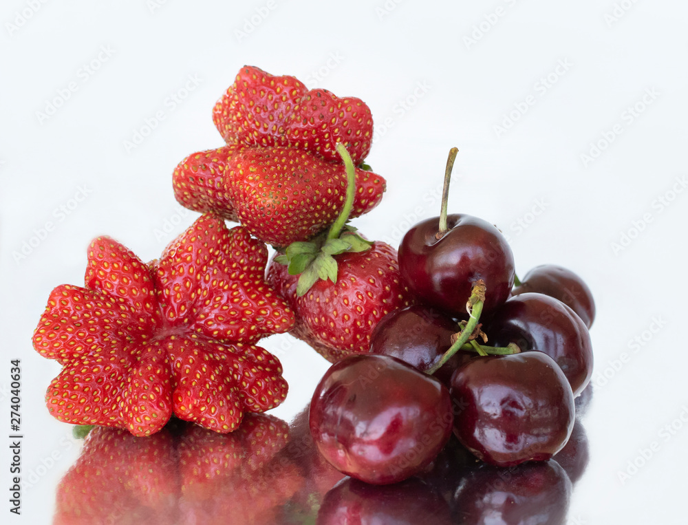 Strawberries of non-standard shapes and cherries on a white background and their reflection in foil. Strawberries of non-standard shapes and cherries on a white background and their reflection in foil.