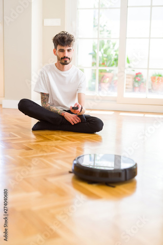 Young man using automatic vacuum cleaner to clean the floor, controling machine housework robot