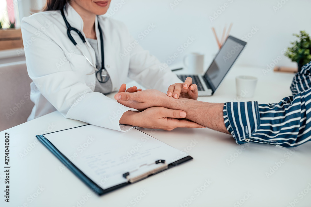 Close-up image of female doctor checking male patient's pulse while sitting at the desk at medical office. Close-up image of female doctor checking male patient's pulse while sitting at the desk at medical office.