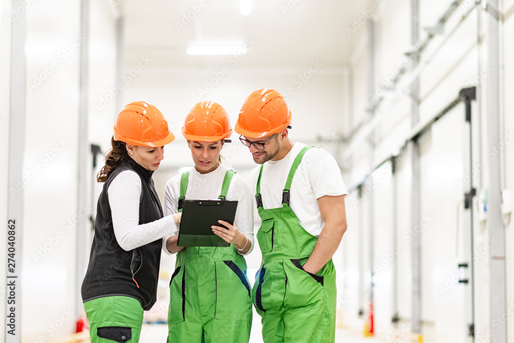 Team of workers in protective workwear discussing and looking a t clipboard indoors. Team of workers in protective workwear discussing and looking a t clipboard indoors.