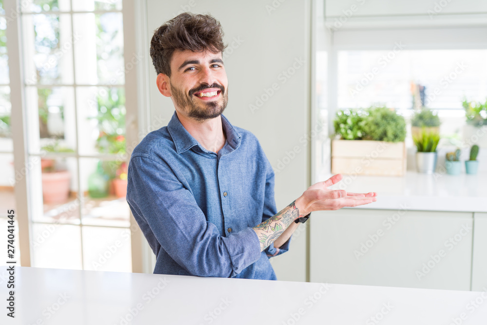 Young man wearing casual shirt sitting on white table Pointing to the side with hand and open palm, presenting ad smiling happy and confident