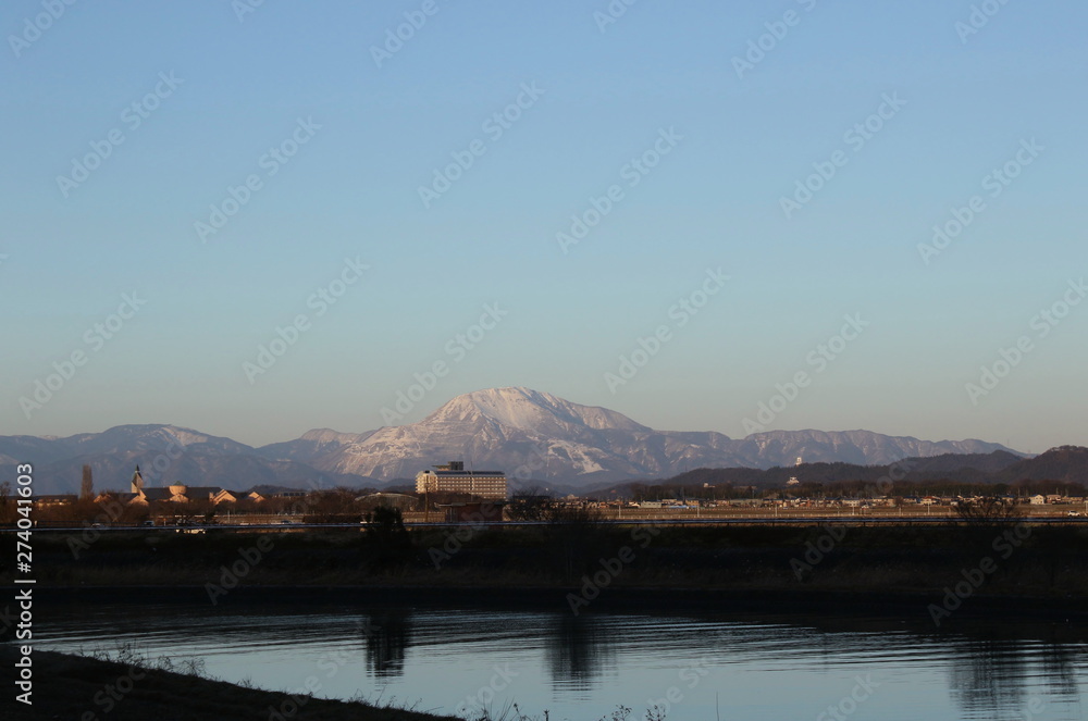 雪化粧した伊吹山と滋賀県彦根市の宇曽川と遠くにある町並みの様子です