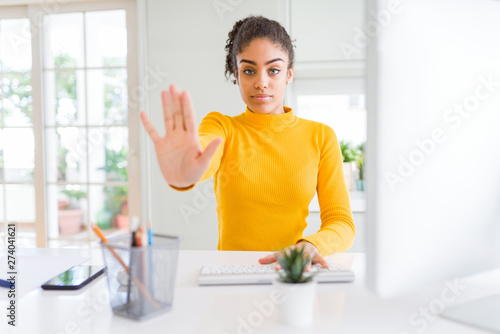 Young african american girl working using computer with open hand doing stop sign with serious and confident expression, defense gesture