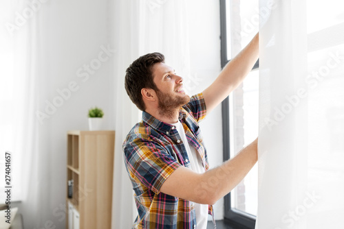 people concept - young man opening window curtain at home