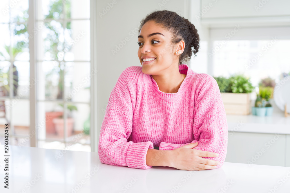 Beautiful african american woman with afro hair wearing casual pink sweater looking away to side with smile on face, natural expression. Laughing confident. Beautiful african american woman with afro hair wearing casual pink sweater looking away to side with smile on face, natural expression. Laughing confident.