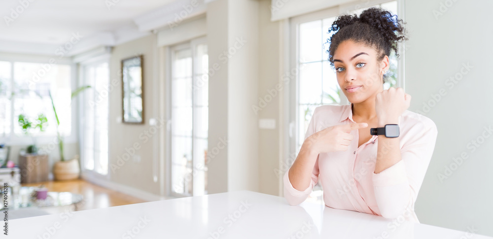 Wide angle of beautiful african american woman with afro hair In hurry pointing to watch time, impatience, looking at the camera with relaxed expression Wide angle of beautiful african american woman with afro hair In hurry pointing to watch time, impatience, looking at the camera with relaxed expression