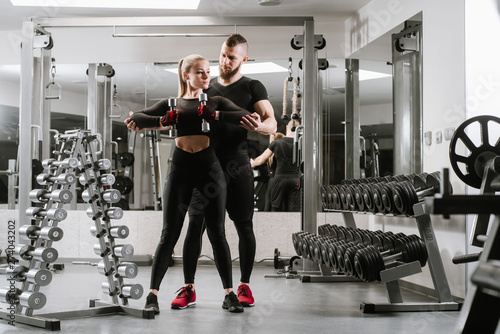 Fitness girl lifting dumbbell with her personal coach in the gym