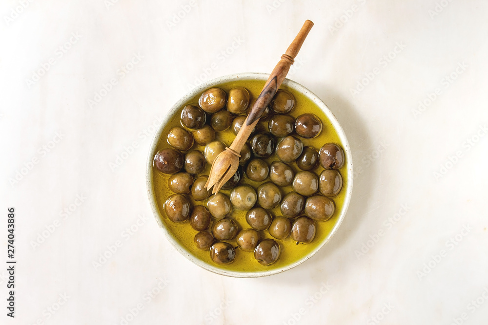Ceramic plate of green whole olives in olive oil over white marble background. Flat lay, space Ceramic plate of green whole olives in olive oil over white marble background. Flat lay, space
