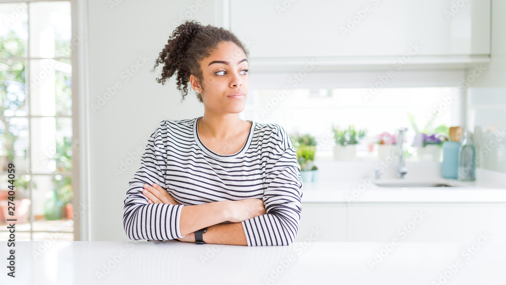 Beautiful african american woman with afro hair wearing casual striped sweater looking to the side with arms crossed convinced and confident Beautiful african american woman with afro hair wearing casual striped sweater looking to the side with arms crossed convinced and confident