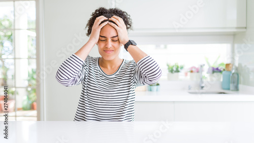 Beautiful african american woman with afro hair wearing casual striped sweater suffering from headache desperate and stressed because pain and migraine. Hands on head.