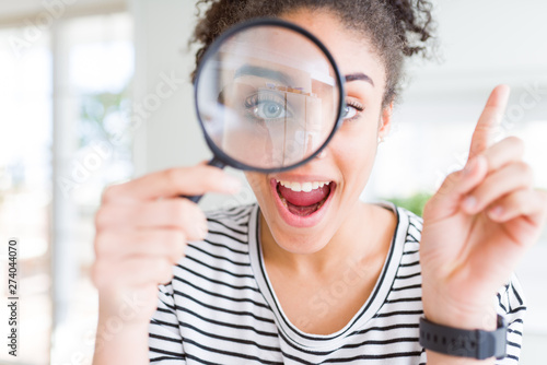 Young african american woman looking through magnifying glass very happy pointing with hand and finger to the side