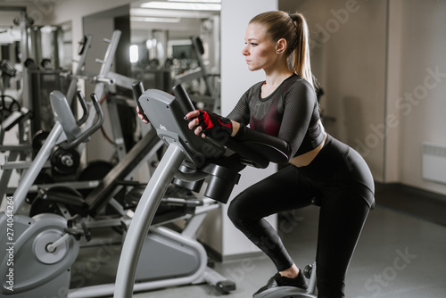 Sports young woman using exercise bike at the gym