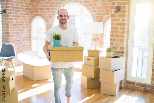 Young handsome man moving to a new house, holding cardboxes smiling very happy for new apartment