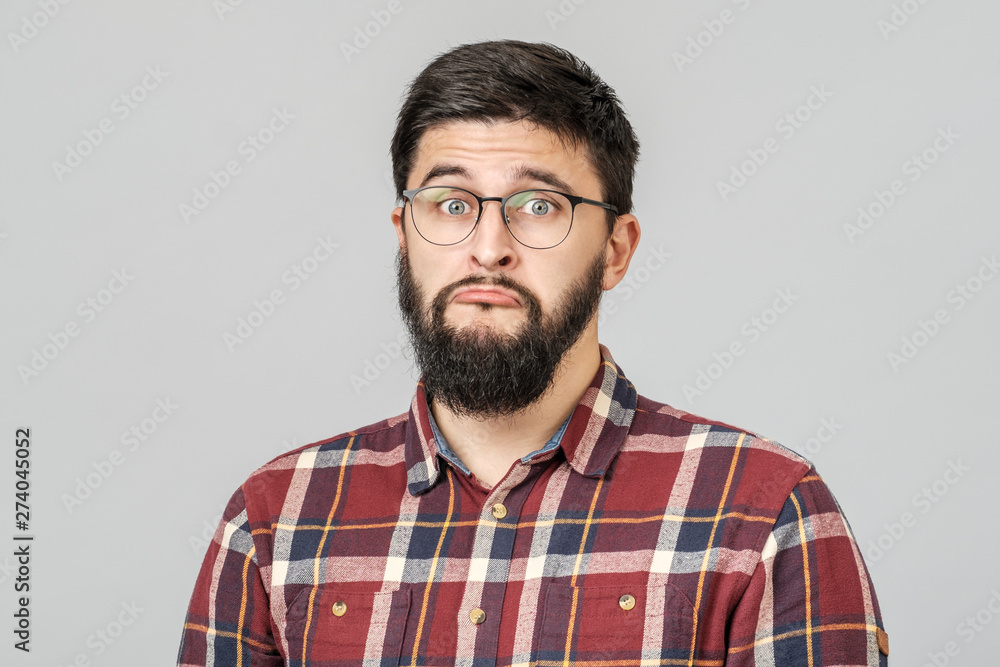 Obraz premium Portrait of unhappy determined european male with serious and worried look against gray background