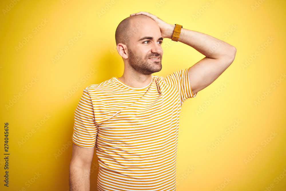 Young bald man with beard wearing casual striped t-shirt over yellow isolated background smiling confident touching hair with hand up gesture, posing attractive and fashionable Young bald man with beard wearing casual striped t-shirt over yellow isolated background smiling confident touching hair with hand up gesture, posing attractive and fashionable