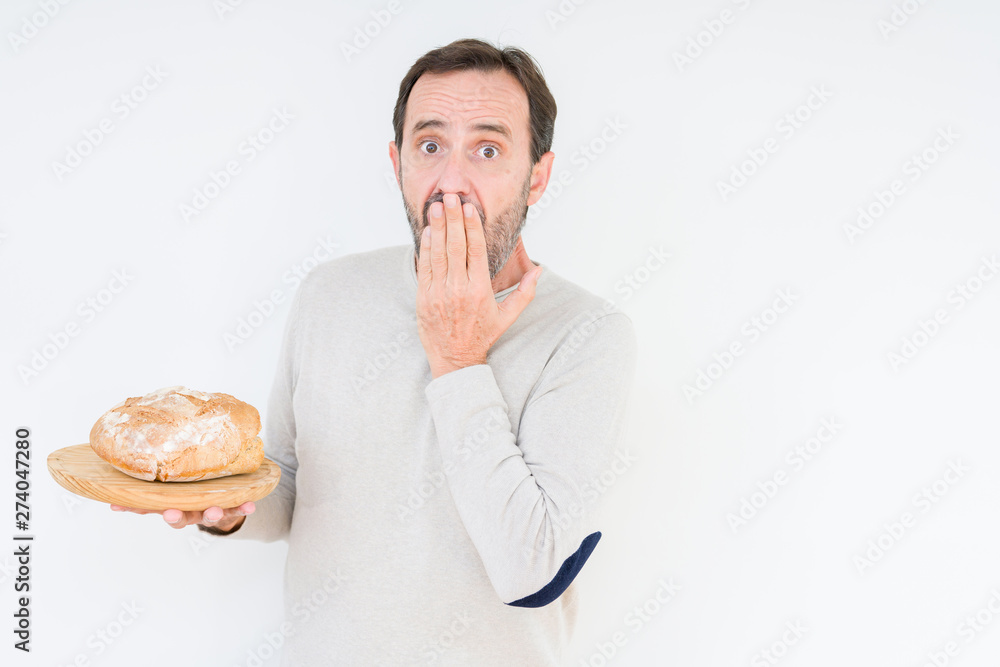 Senior man holding homemade fresh bread over isolated background cover mouth with hand shocked with shame for mistake, expression of fear, scared in silence, secret concept Senior man holding homemade fresh bread over isolated background cover mouth with hand shocked with shame for mistake, expression of fear, scared in silence, secret concept