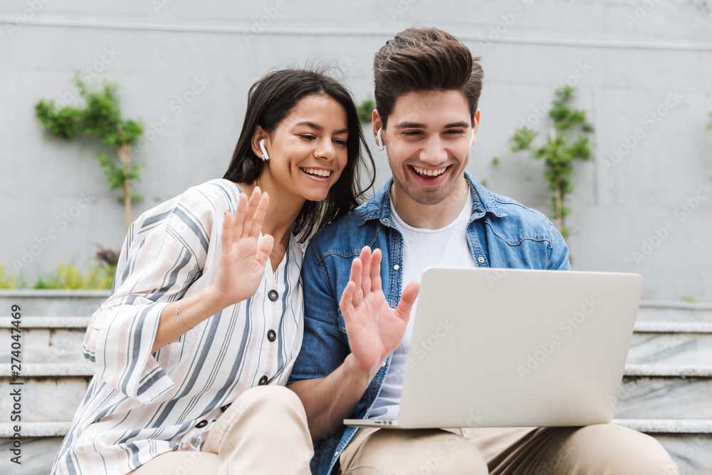 Φωτογραφία Happy young amazing loving couple business people colleagues outdoors outside on steps using laptop computer waving talking with family or friends