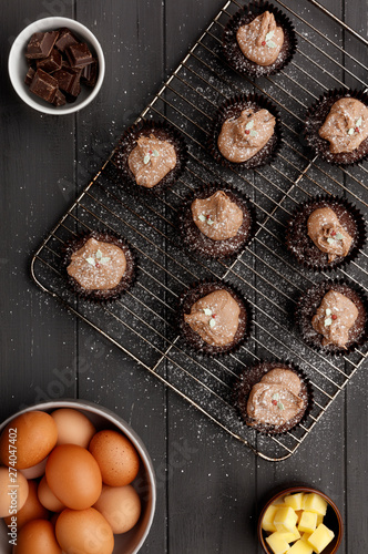 Fairy cakes on a cooling tray with a dusting of icing sugar and ingredients, on a distressed grey wooden background © PHILL THORNTON PHOTO