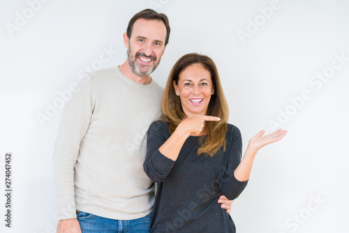 Beautiful middle age couple in love over isolated background amazed and smiling to the camera while presenting with hand and pointing with finger.