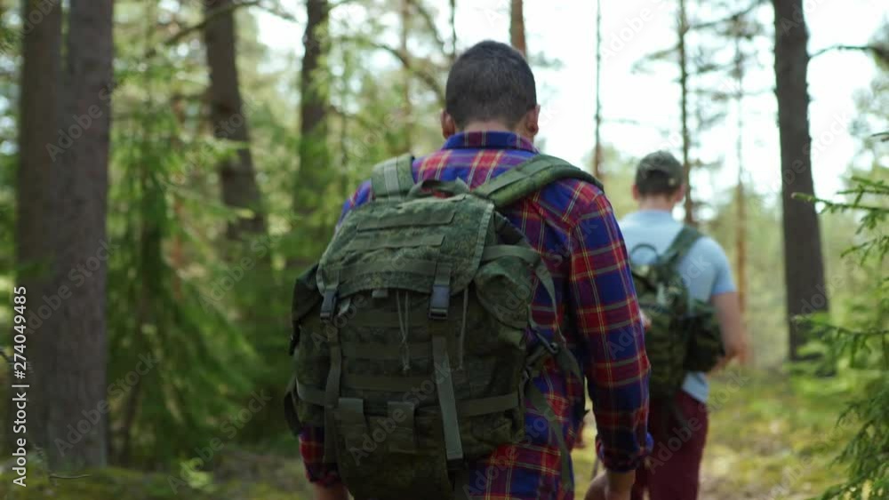 Group of four young hikers with backpacks walking up trail in forest during adventure, rear view follow shot Group of four young hikers with backpacks walking up trail in forest during adventure, rear view follow shot