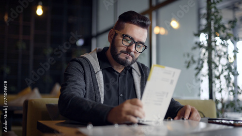 Stylish guy with beard in glasses came in restaurant and choosing food in menu.