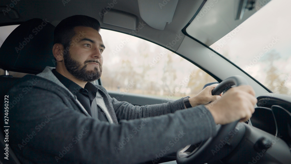 handsome bearded man is driving car in city in daytime, inside side view, guy is holding hands on a steering wheel handsome bearded man is driving car in city in daytime, inside side view, guy is holding hands on a steering wheel